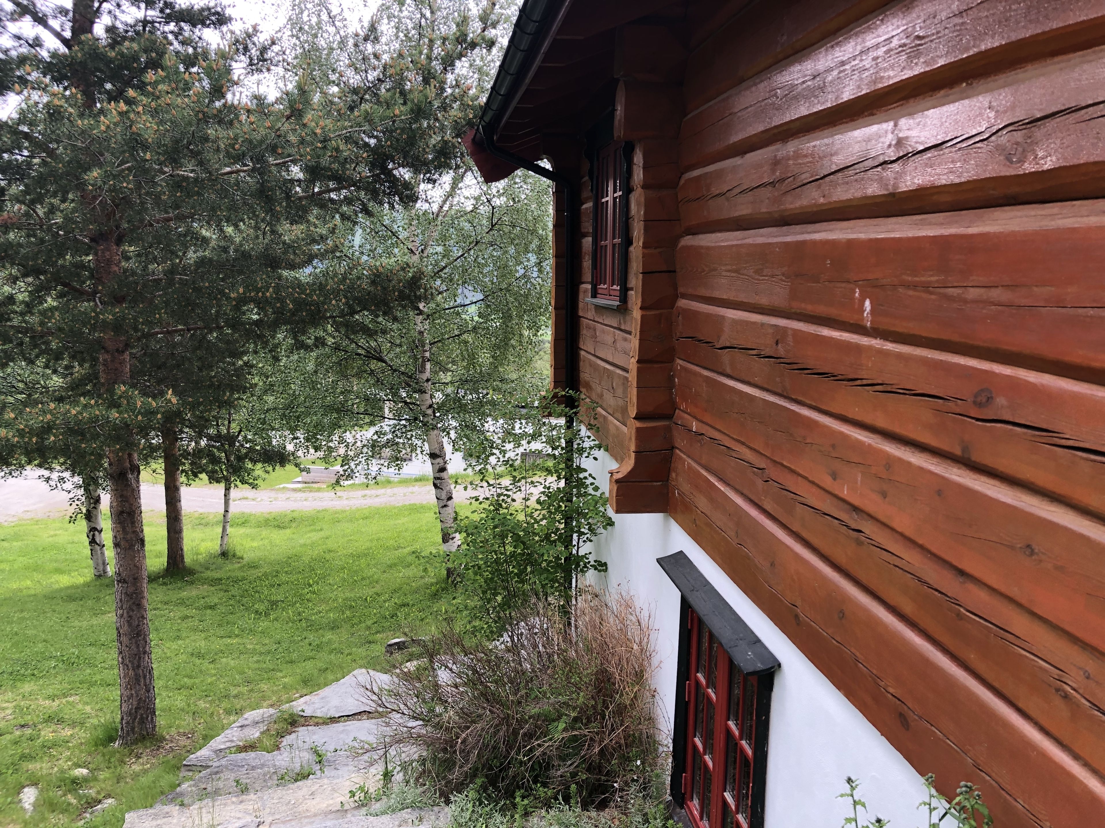Una cabaña de madera con fachada blanca, rodeada de césped y árboles.