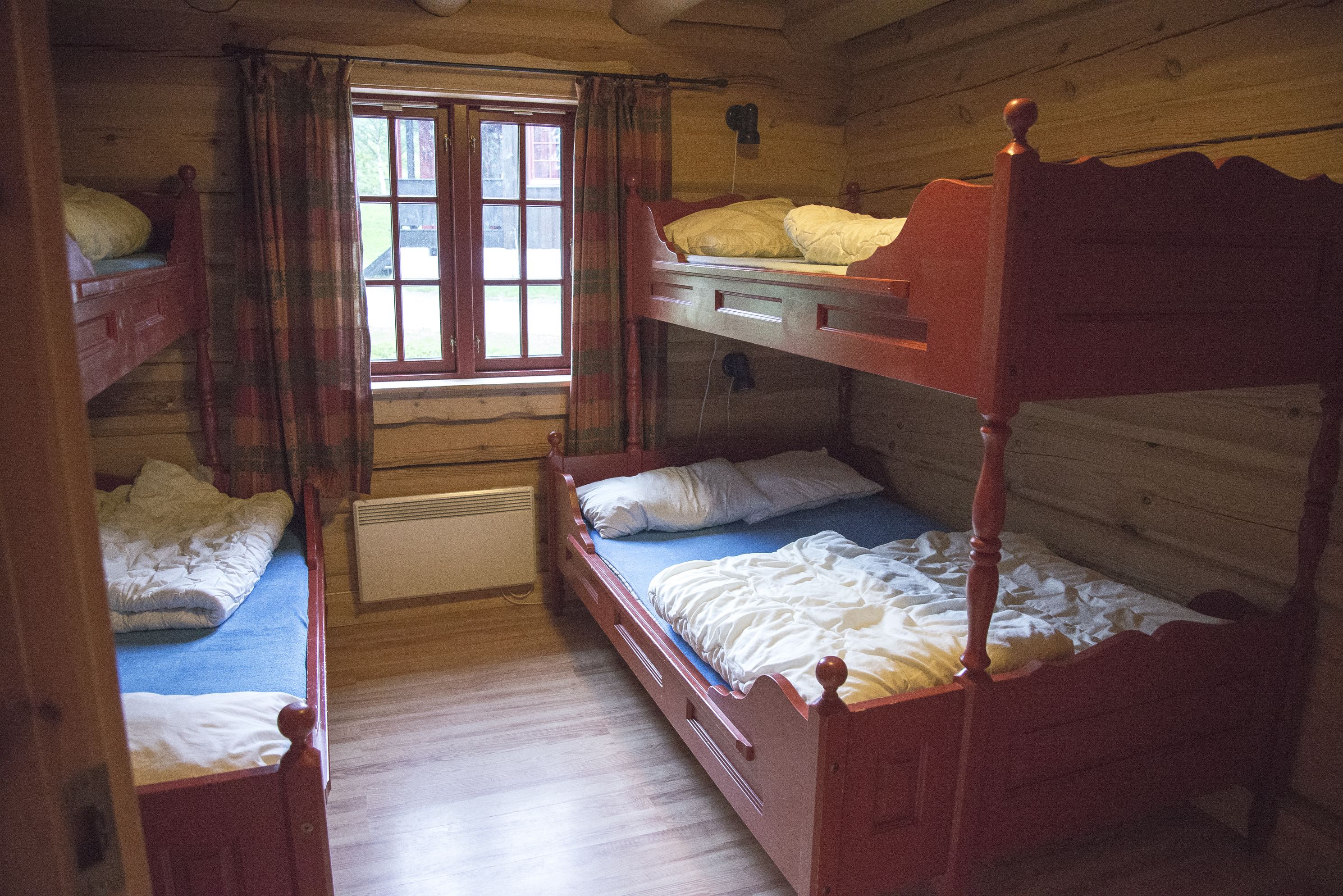 Una cabana amb lliteres, una finestra amb cortines i un interior de fusta.