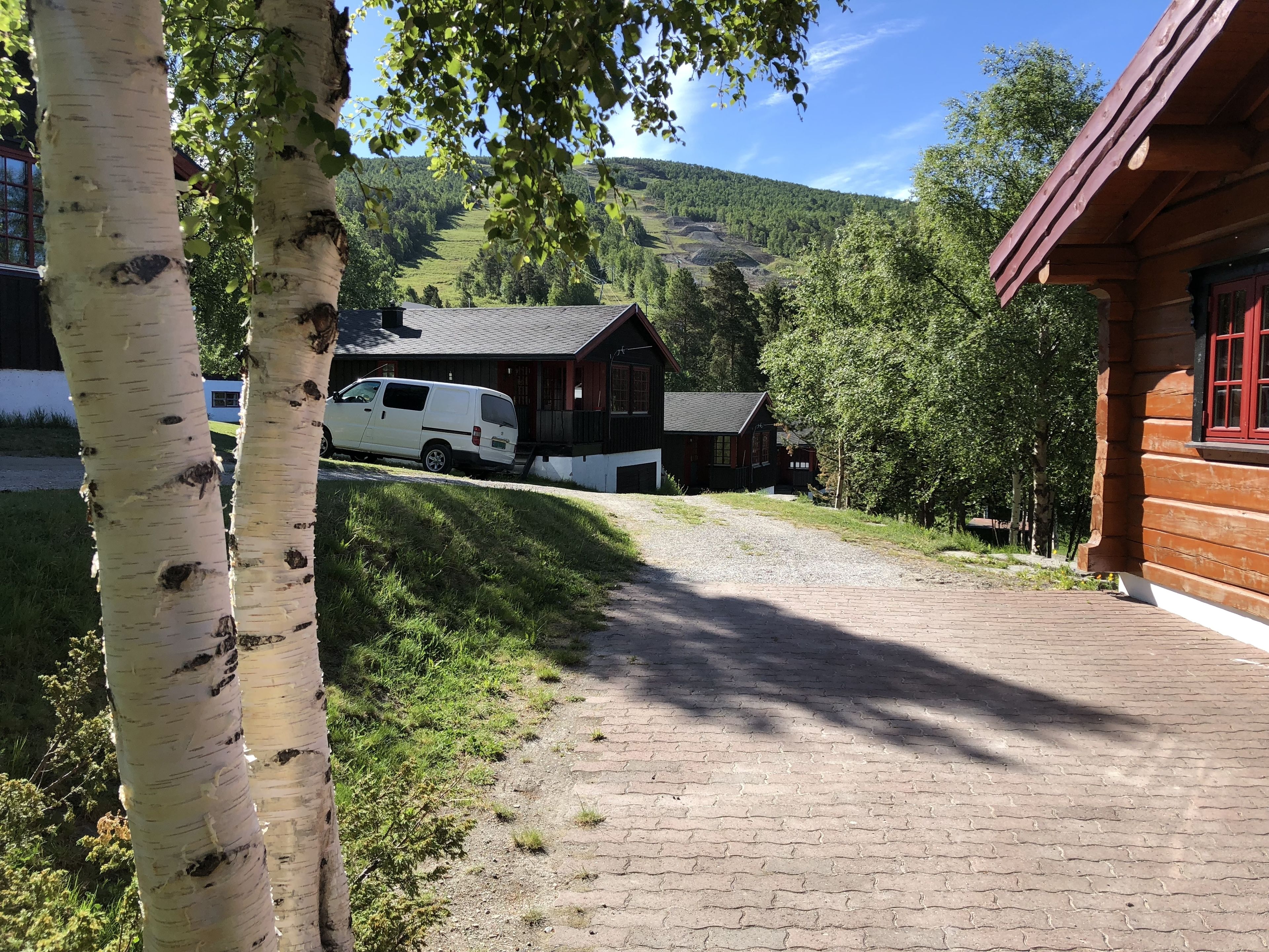 A wooden cabin with a gravel driveway leading to a white van parked in front.