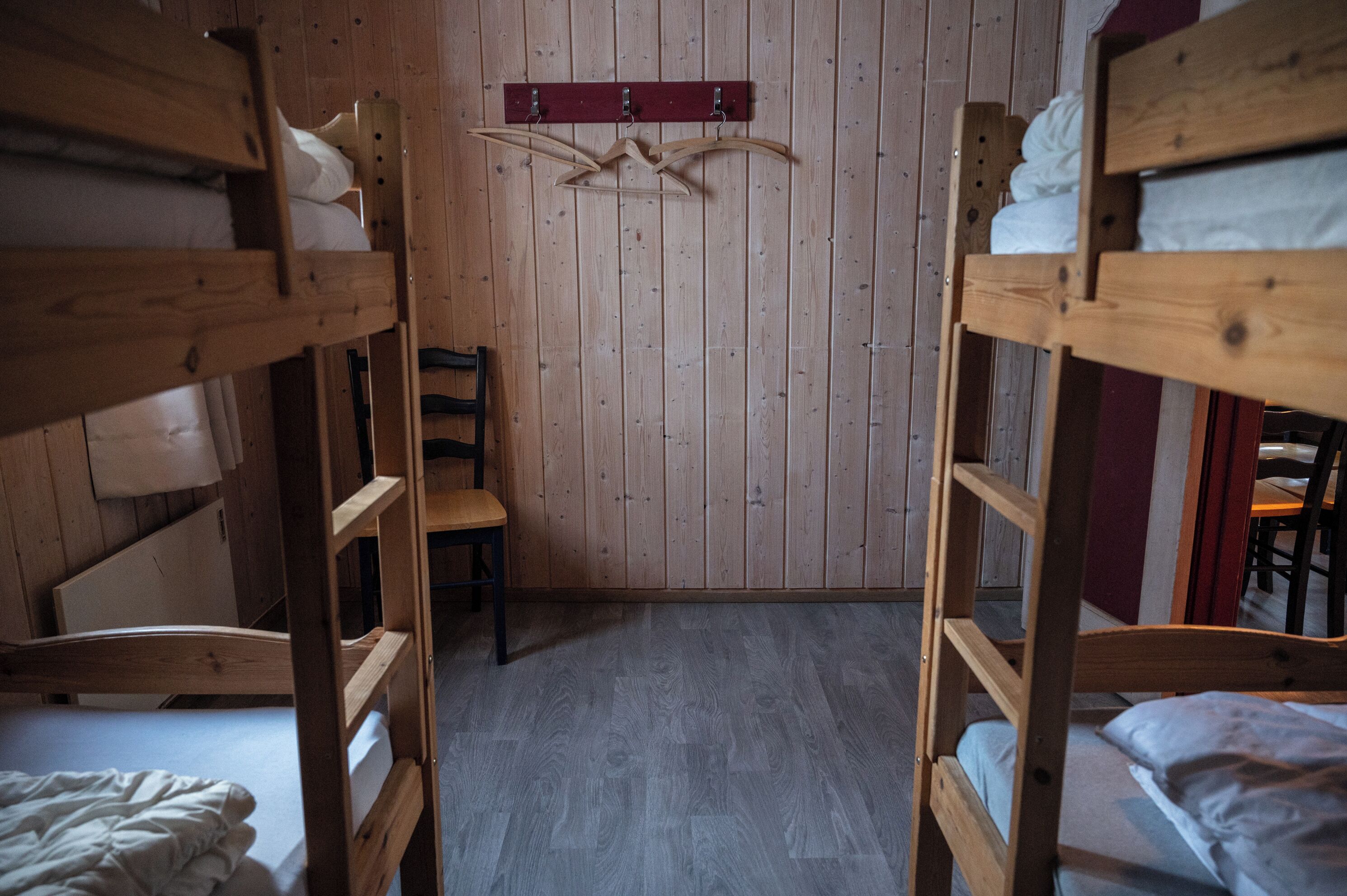 Dormitorio con literas, paredes y pisos de madera, una silla de madera y un perchero.