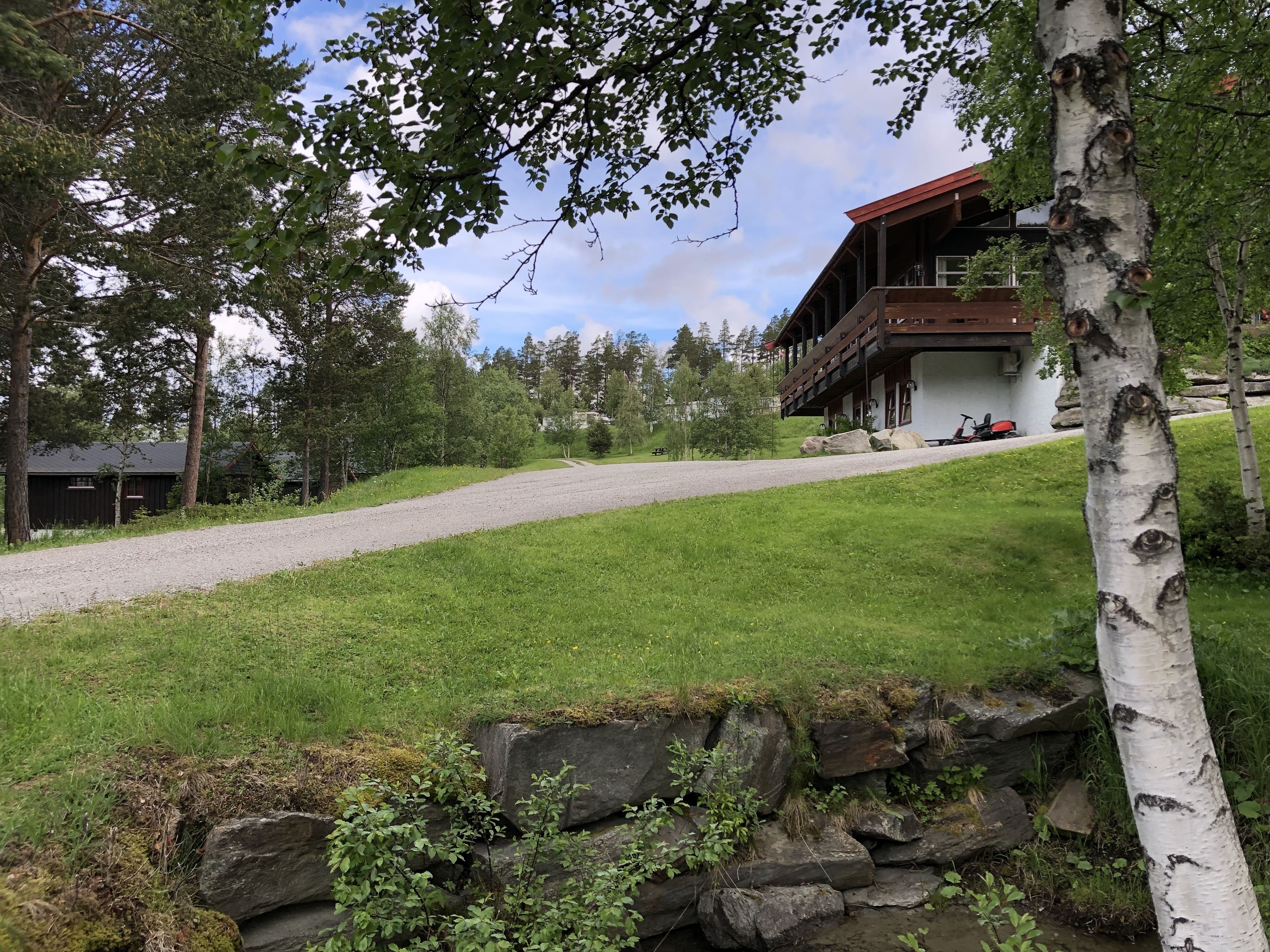 A rustic lodge with a stone wall, a gravel path, and a grassy area.