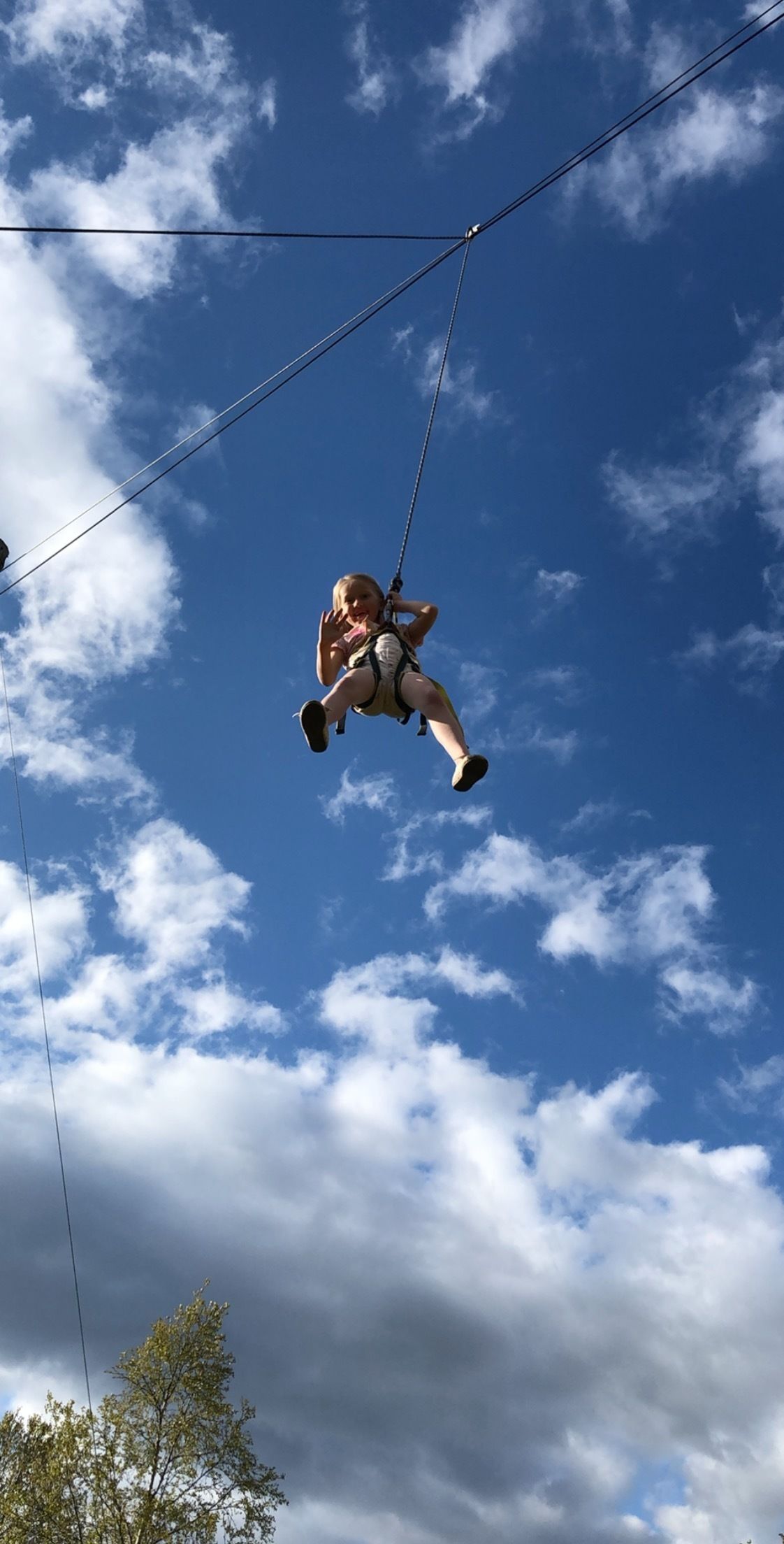 Una persona suspendida en el aire, sujeta a un cable, con un cielo parcialmente nublado de fondo.