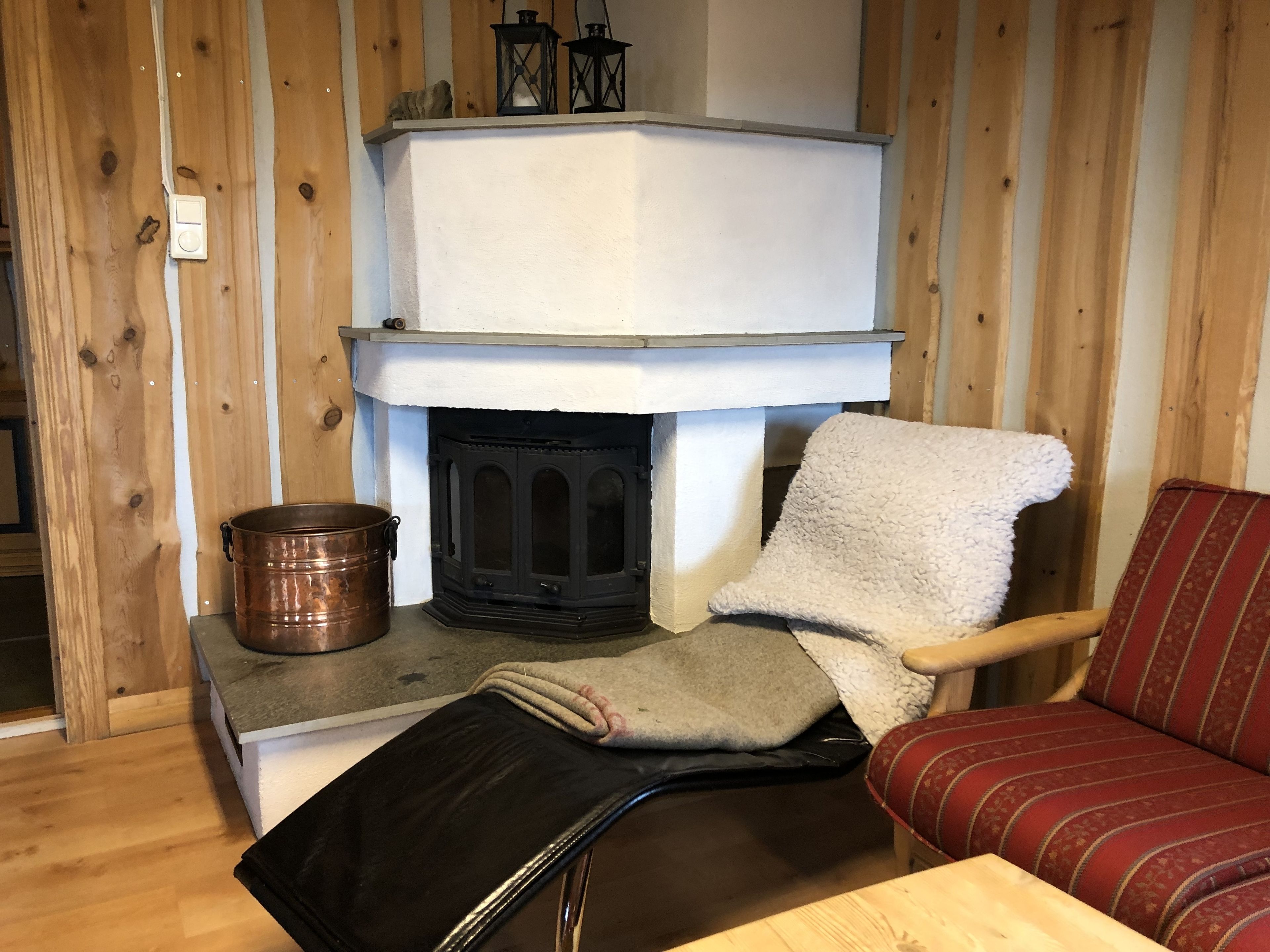 A cozy room with a fireplace, a wooden chair, a red sofa, and a black suitcase on a table.