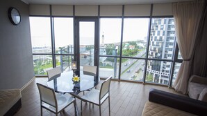Un salon moderne avec une table en verre, deux fauteuils, un canapé et une vue sur le paysage urbain, visible à travers de grandes fenêtres.
