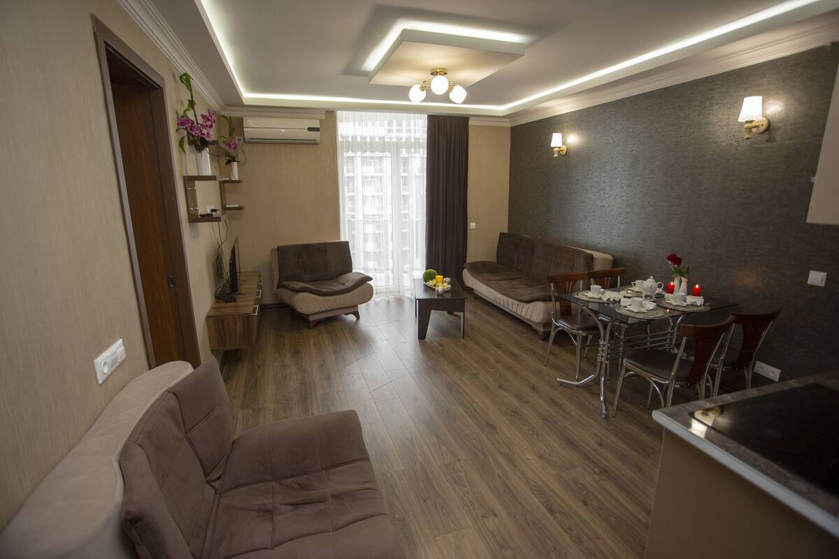 A modern living room with a sofa, chairs, a dining table, and a kitchen area.