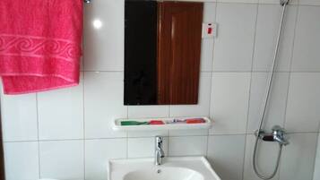 Un baño pequeño con inodoro y lavamanos blancos, un espejo y una ducha.