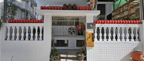 A building entrance with a tiled facade, a balcony with decorative pots, and a signboard.