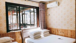 Quarto com duas camas, janela com vista para a rua e ar condicionado na parede.