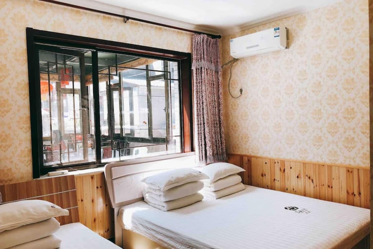 A room with two beds, a window with a view of the street, and an air conditioning unit on the wall.