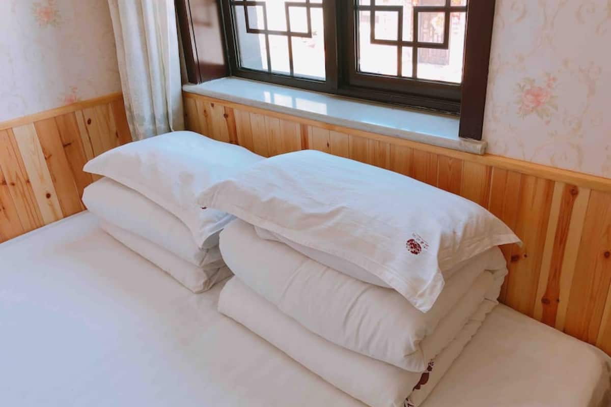 A neatly made bed with white linens in a room with wooden paneling and a window with a grid pattern.
