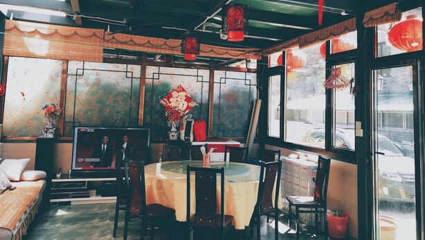 Restaurante com interior tradicional, apresentando uma mesa redonda com toalha de mesa amarela, cadeiras de madeira e lanternas vermelhas penduradas no teto.