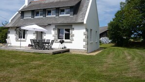 A two-story house with a sloped roof, a patio with outdoor furniture, and a large umbrella. - Country house 5 kms from the sea, 12 kms from Perros Guirec.  (Trelevern)