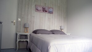 A bedroom with a wooden wall panel, a bed with a white comforter, two bedside tables with lamps, and a picture above the bed. - Country house 5 kms from the sea, 12 kms from Perros Guirec.  (Trelevern)