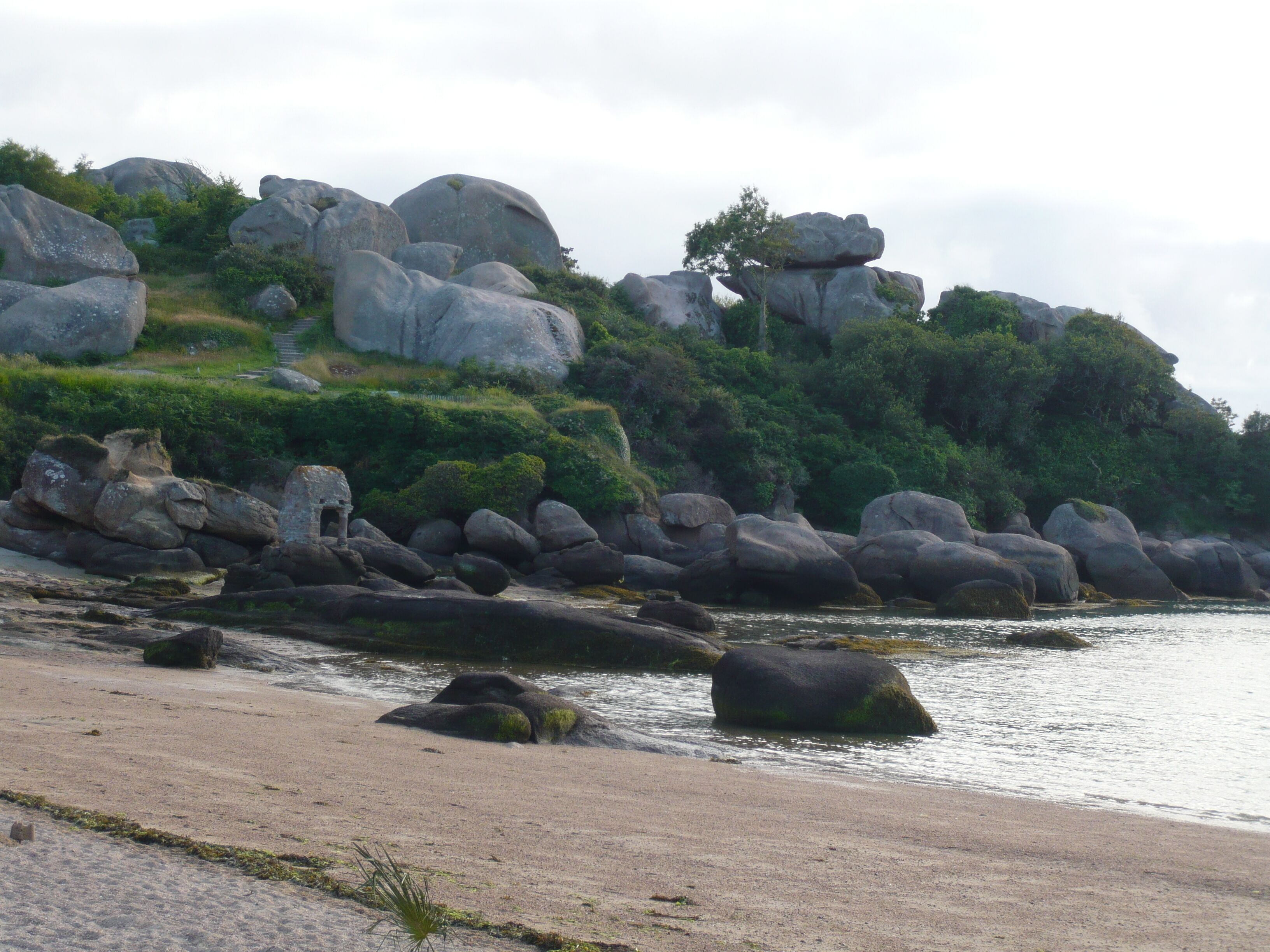 Un paisaje costero con grandes rocas, una playa arenosa y abundante vegetación.