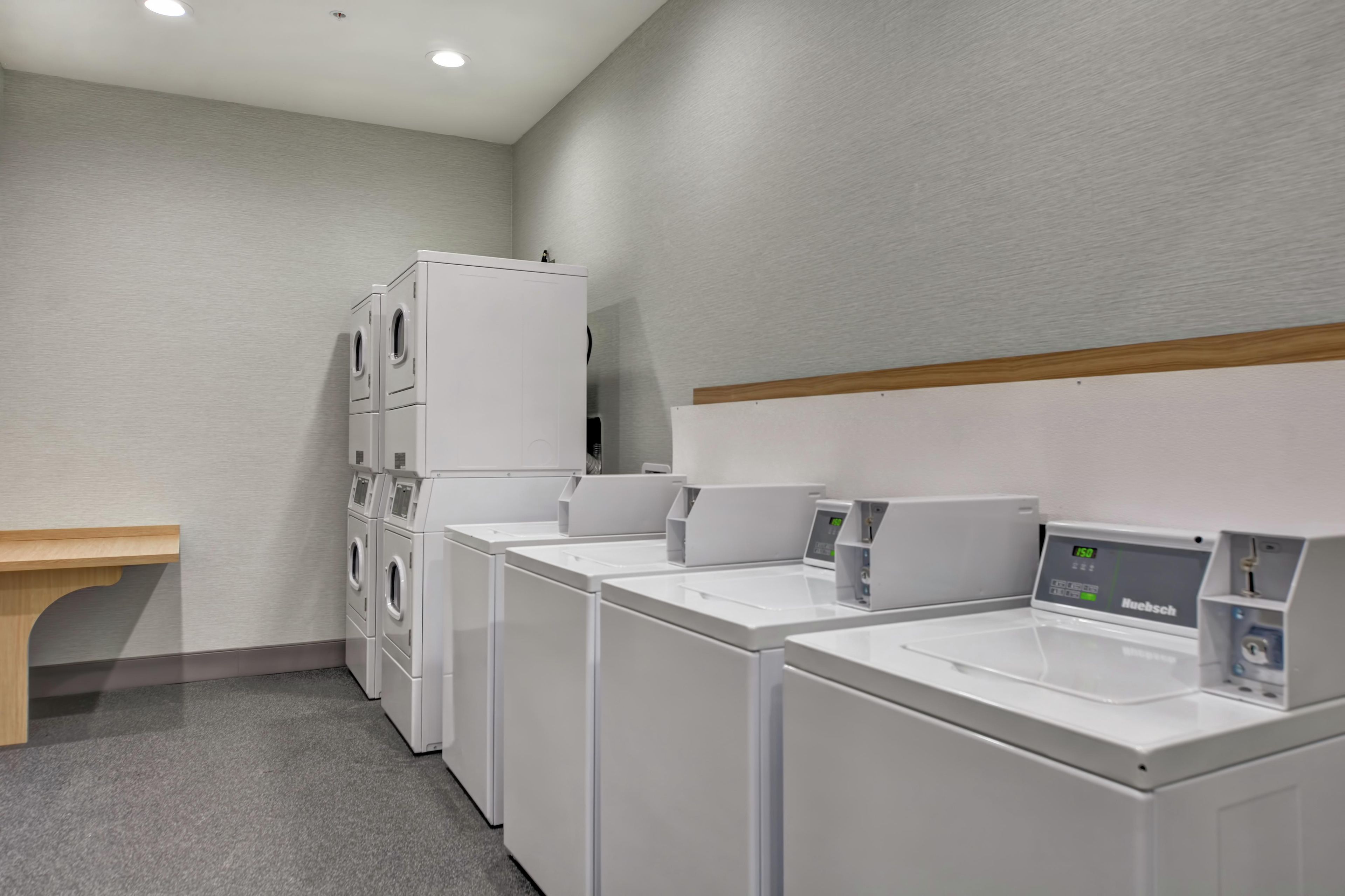 A laundry facility with multiple washing machines and dryers, a wooden bench, and a wall-mounted control panel.