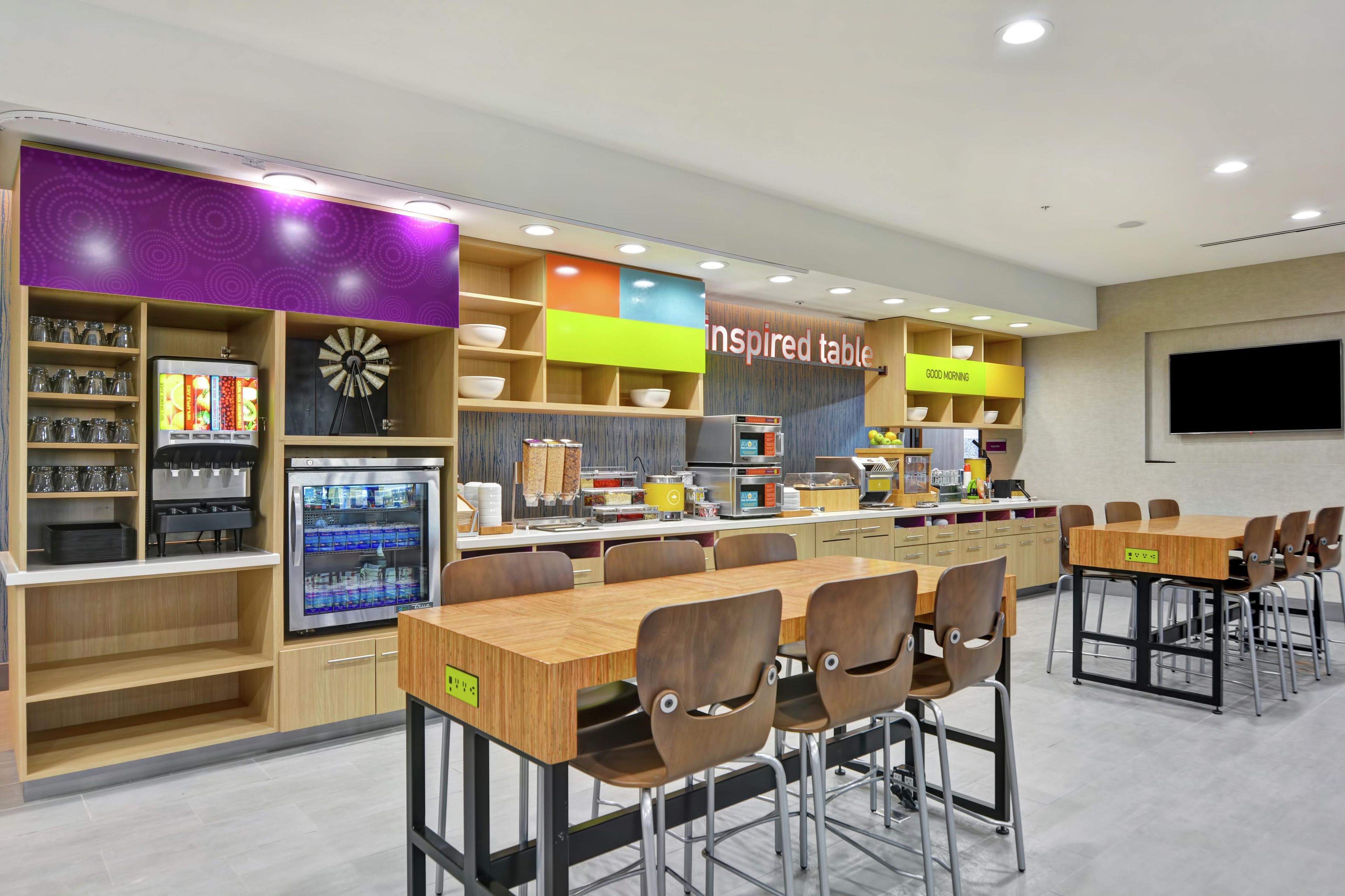 Una cafetería moderna con varias zonas de estar, una estación de autoservicio para bebidas y diversas opciones de comida.