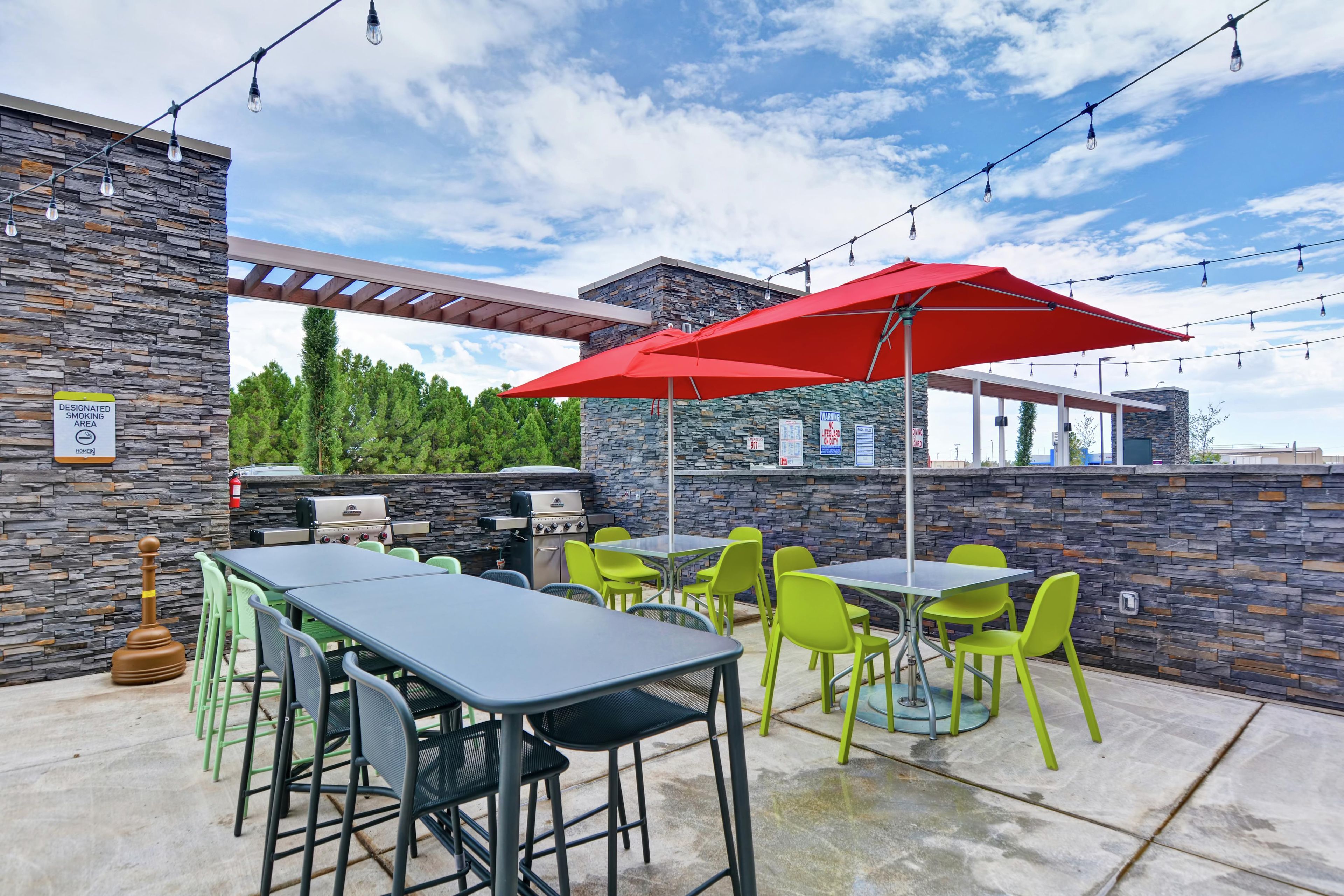 En udendørs terrasse med borde og stole, en rød parasol og en stenvæg.