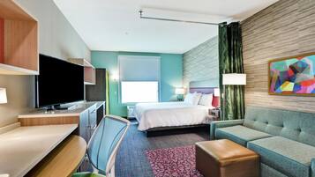 A modern hotel room with a bed, seating area, TV, and a painting on the wall.