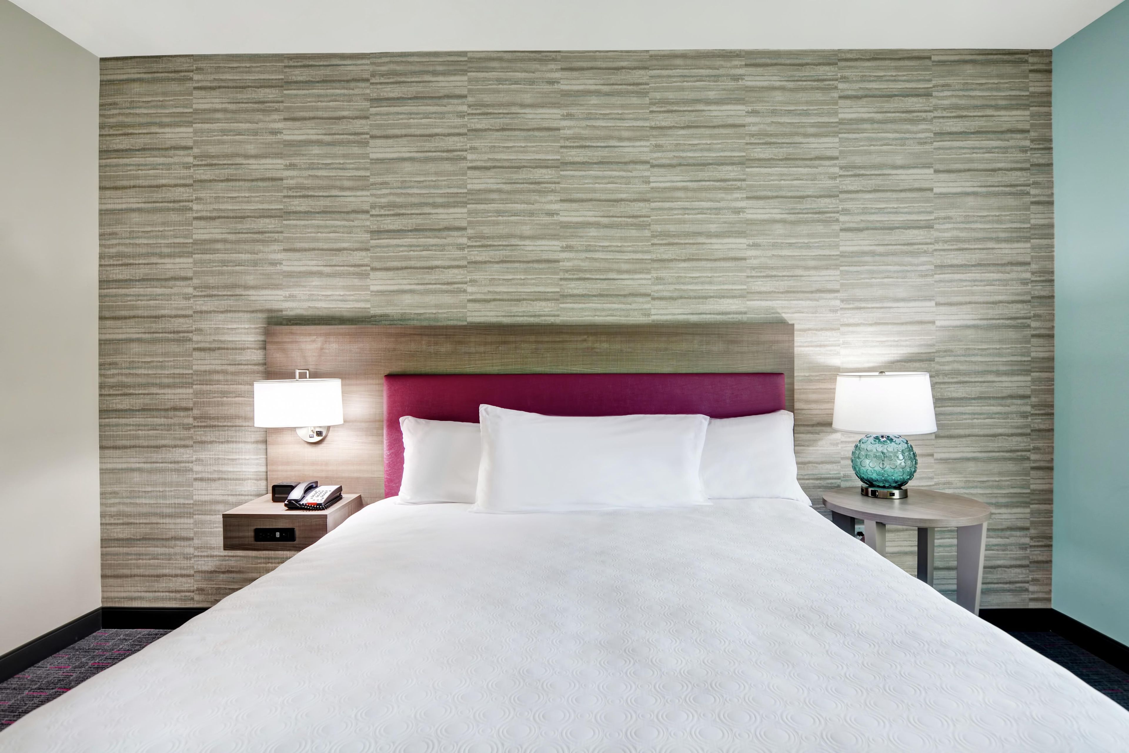 Une chambre d’hôtel avec un grand lit, deux tables de chevet, une tête de lit et un mur à motifs.