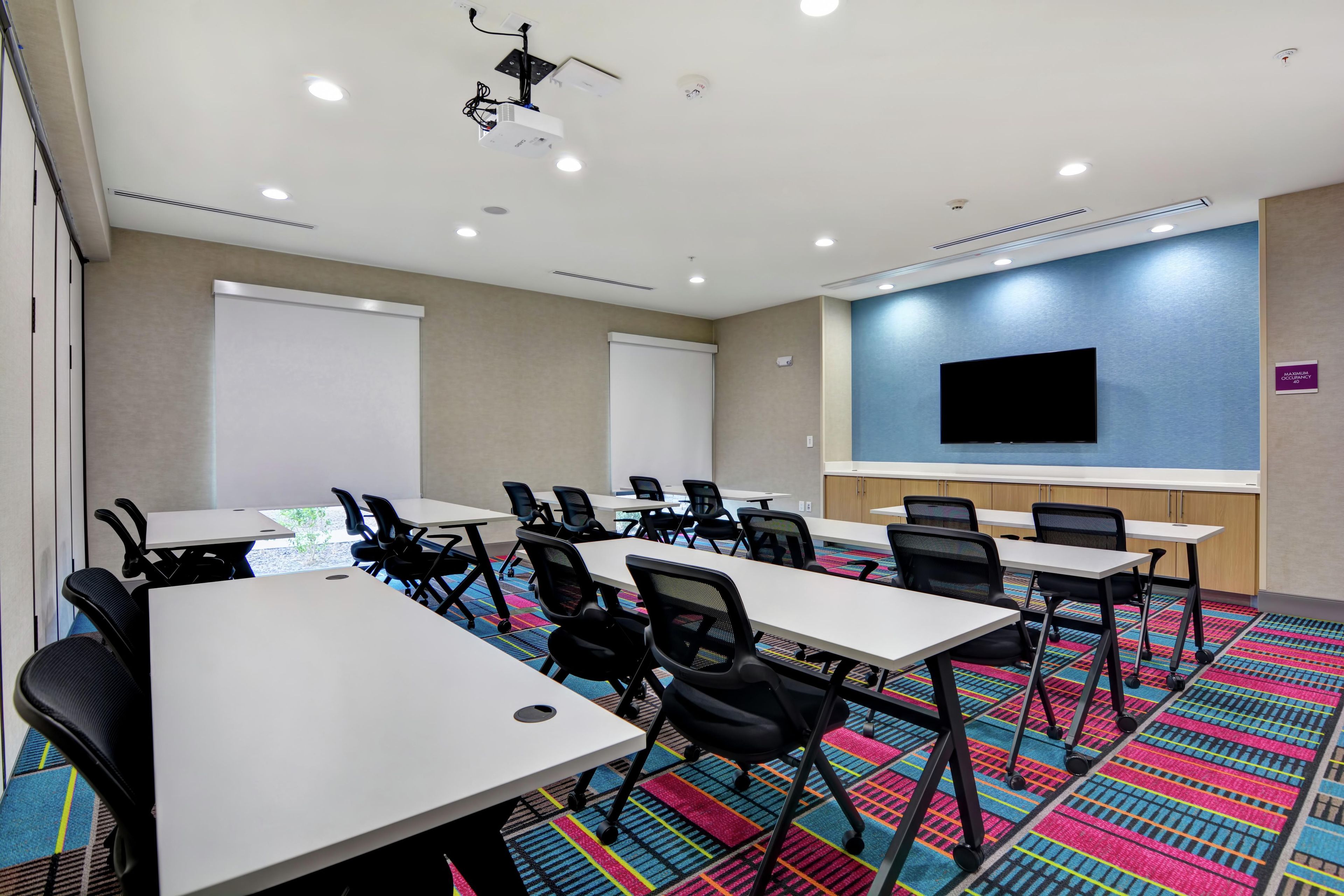 A conference room with white tables, black chairs, a projector, and a large screen.