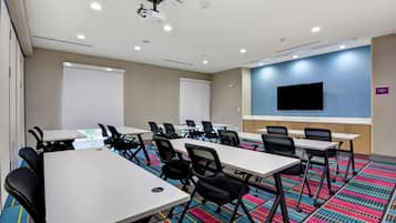 A conference room with white tables, black chairs, a projector, and a large screen.