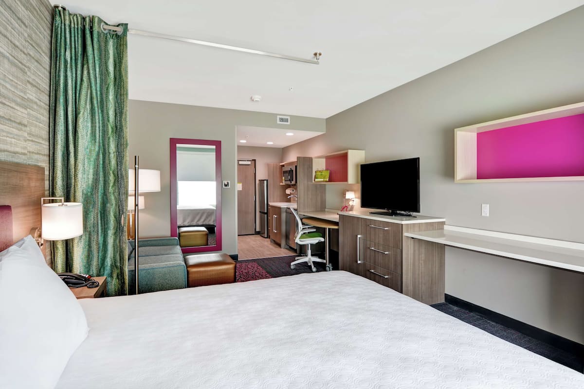 Une chambre d’hôtel avec un grand lit, un bureau avec une chaise, une télévision et une petite kitchenette.