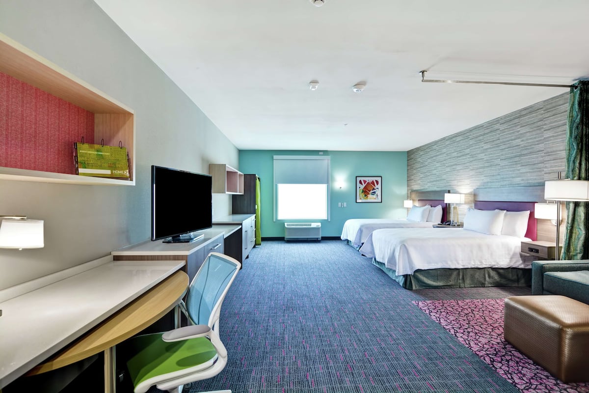 Une chambre d’hôtel avec un bureau, deux lits, une télévision, une chaise et une fenêtre.