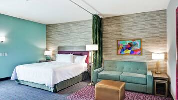 Una habitación de hotel con cama, sofá, una mesita, lámpara y un cuadro abstracto colorido en la pared.