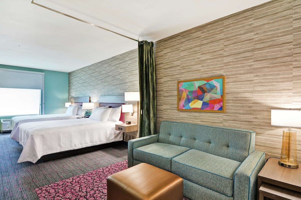 Une chambre d’hôtel avec deux lits, un canapé, un petit pouf, une lampe et un tableau au mur.