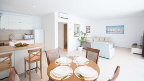 A modern kitchen with white cabinets, a microwave, and a dining area with a wooden table set for four. - Apartments Horizon (Dubrovnik)