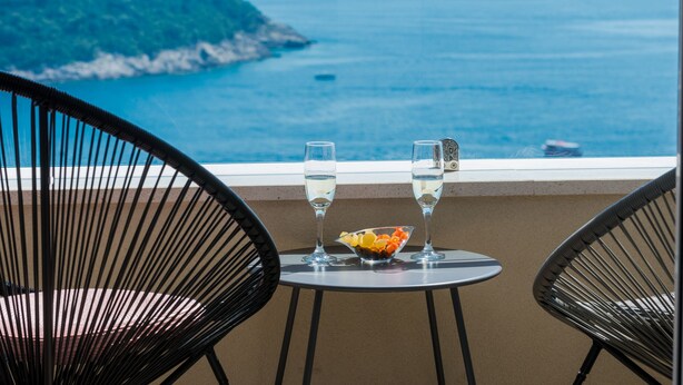 A table with two glasses of water and a bowl of fruit, overlooking a coastal view. - Apartments Horizon (Dubrovnik)
