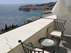A balcony with two chairs and a small table, overlooking a coastal town with historic buildings and a harbor. - Apartments Horizon (Dubrovnik)