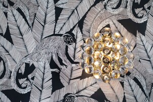 A chandelier with multiple clear glass bulbs and a geometric metal base, set against a black background with silver leaf-like patterns.