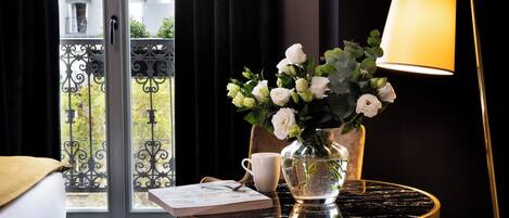 Una habitación con vista a un balcón, una mesa con un florero, una taza y un libro.