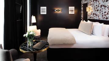 A modern hotel room with a large bed, a round table with a laptop, a chair, and a vase of flowers.