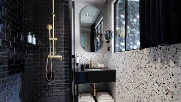 Une salle de bain moderne avec des murs recouverts de carreaux noirs, une baignoire sur pieds, un meuble-lavabo noir avec un miroir et une fenêtre donnant sur un jardin fleuri.