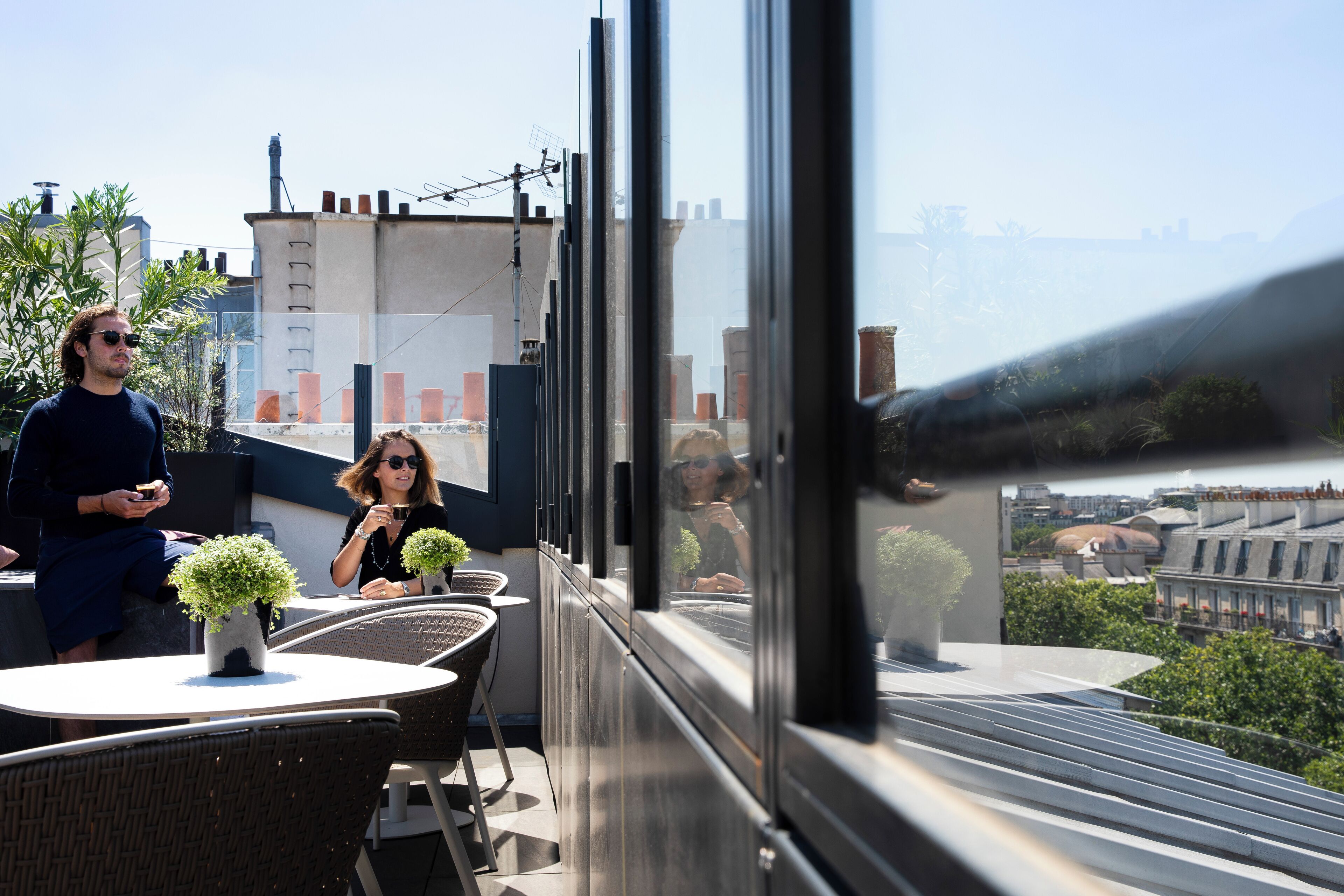 Una terraza en la azotea con mobiliario exterior, vistas a la ciudad y un amplio ventanal.