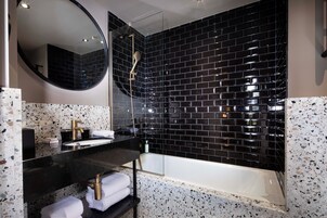 A modern bathroom with a black tiled wall, a round mirror, a black countertop, a white sink, and a bathtub.