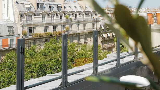 A rooftop terrace with a view of the Eiffel Tower, featuring a table and chairs, and a railing.