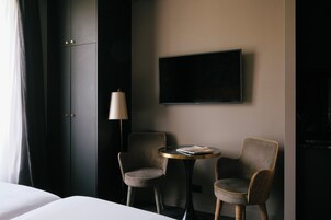 Ένα δωμάτιο ξενοδοχείου με ένα κρεβάτι, δύο πολυθρόνες, ένα μικρό στρογγυλό τραπέζι, μια τηλεόραση τοποθετημένη στον τοίχο και ένα φωτιστικό.