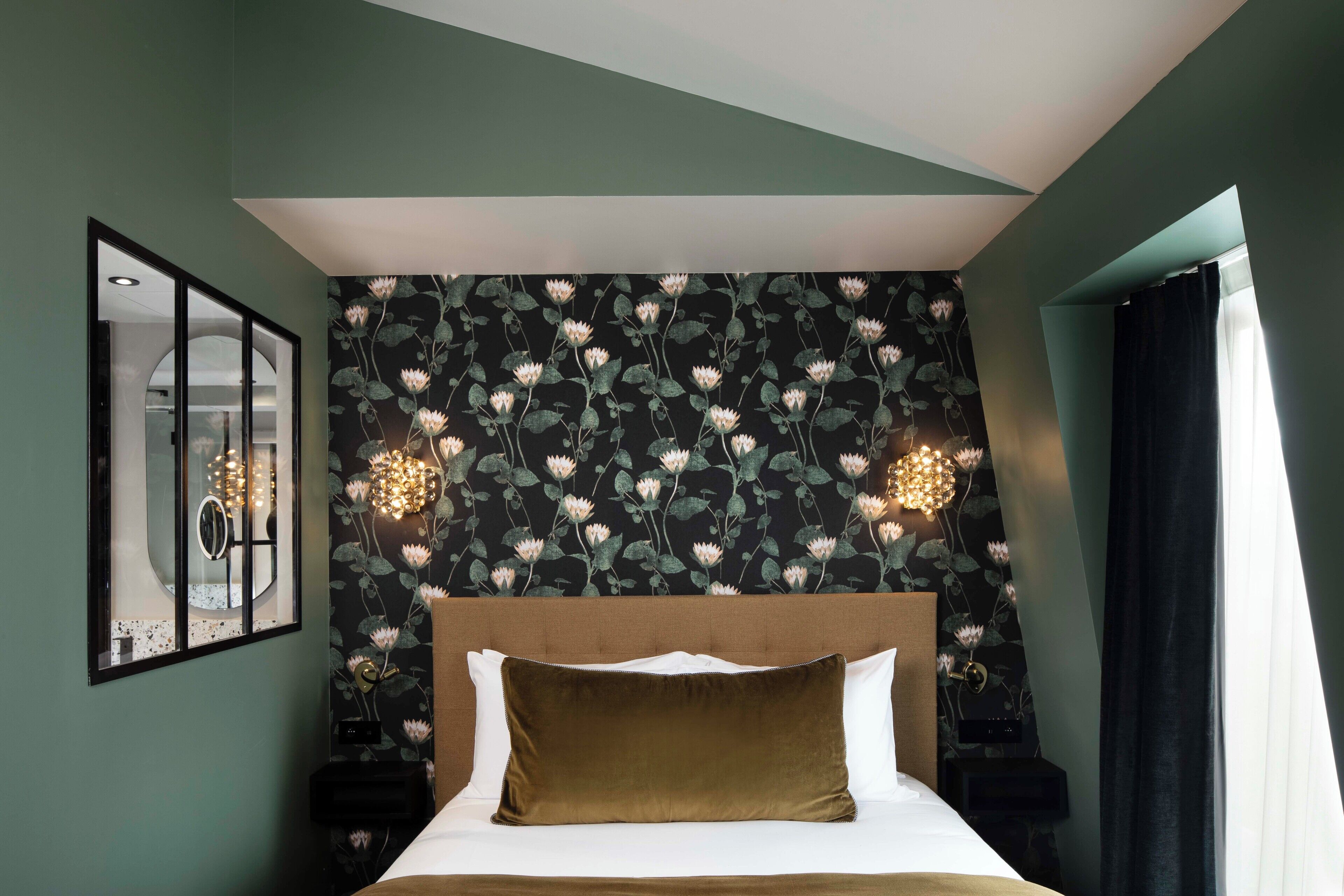 Quarto com papel de parede floral, uma cama grande, um espelho e uma mesa de cabeceira com abajur.