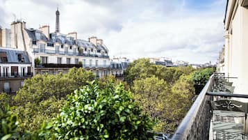 Une vue sur les bâtiments parisiens, avec la Tour Eiffel en arrière-plan, un balcon avec une balustrade et de luxuriants arbres verdoyants.