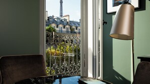 A room with a view of the Eiffel Tower, a balcony with wrought iron railing, a table with a book, and a lamp.
