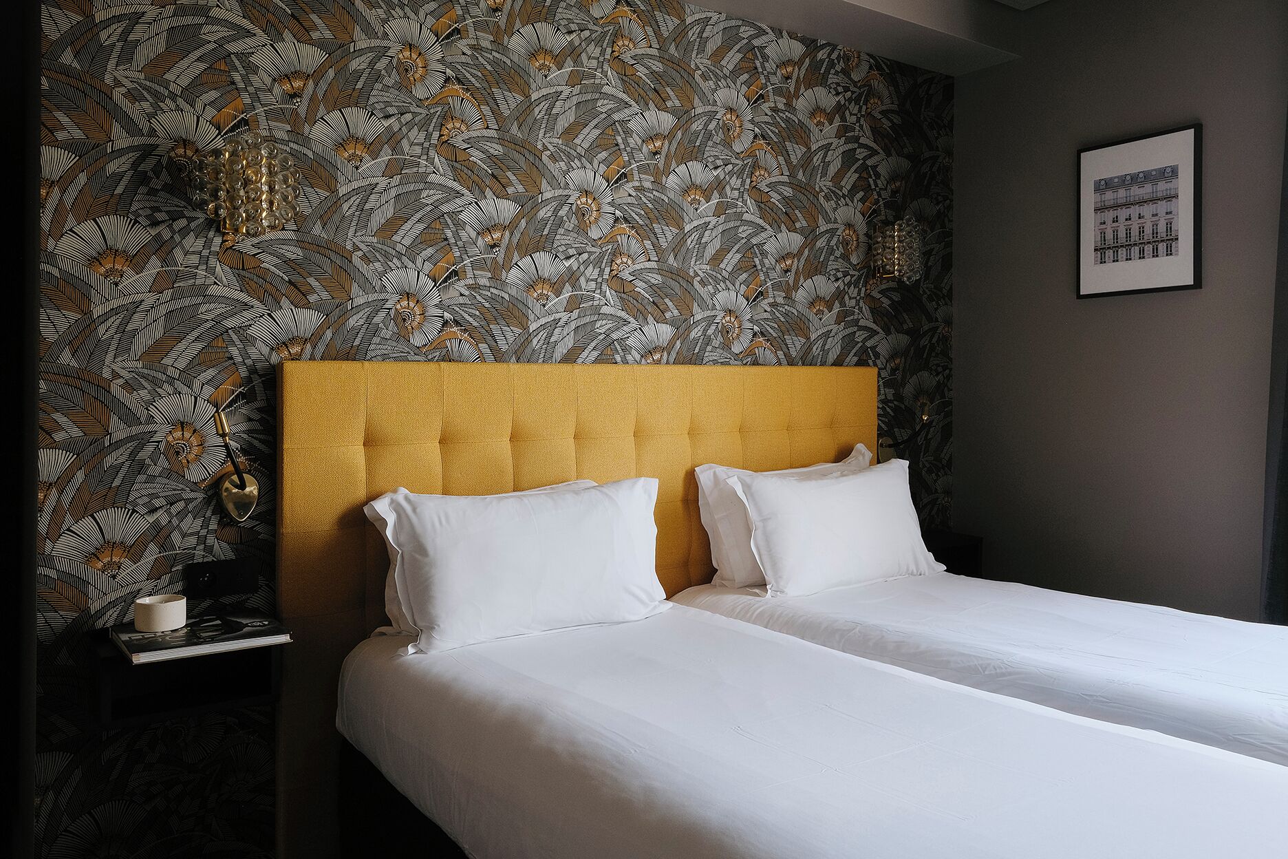A hotel room with a bed, a nightstand, and a wall with a leaf pattern.