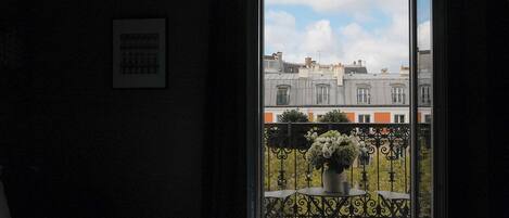 A hotel room with a large window, a bed, and a balcony with a table and chairs.