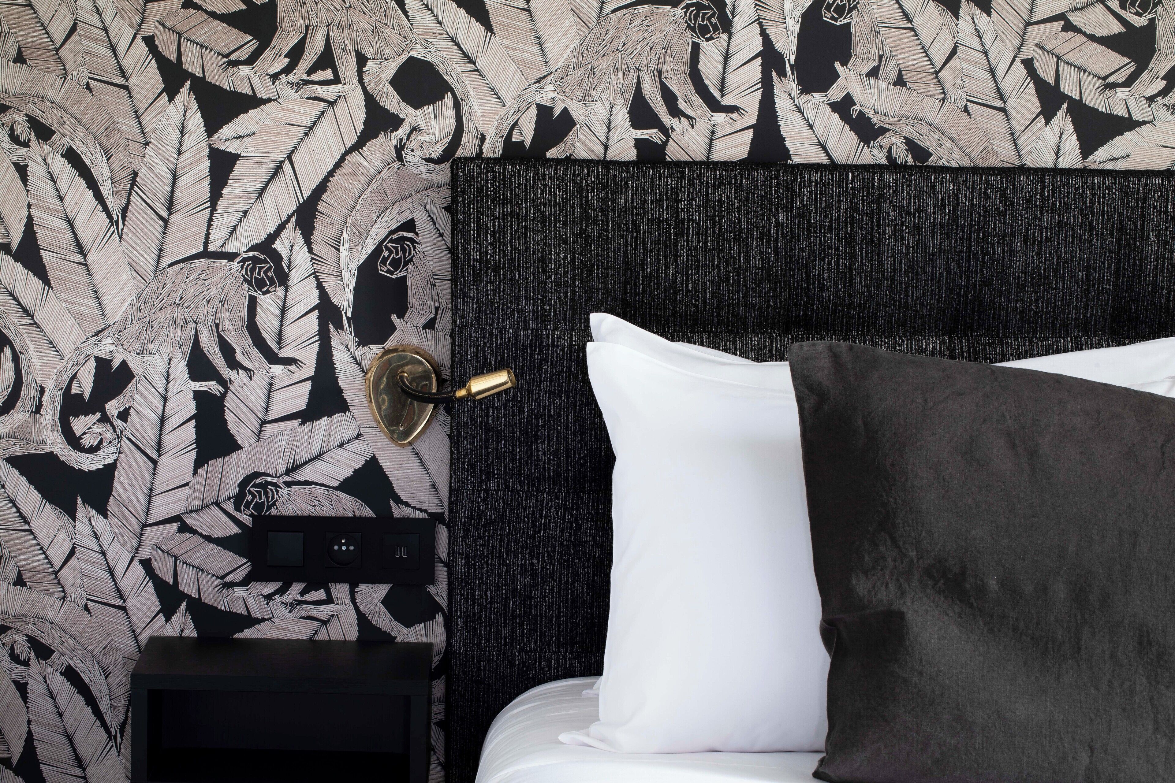 Una cama bien hecha con almohadas blancas y oscuras, un cabecero negro y una pared con un diseño de hojas.