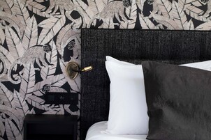 A neatly made bed with white and dark pillows, a black headboard, and a wall with a leaf pattern.