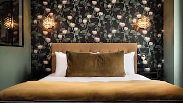 Een net opgemaakt bed met een bruin hoofdeinde, witte kussens en een bruine plaid. Aan beide zijden van het bed zijn wandlampen bevestigd.