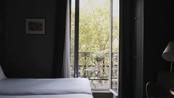 A hotel room with a bed, a chair, and a balcony with a table and flowers.