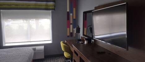 Habitación de hotel con cama, escritorio, televisor de pantalla plana, silla y ventana grande.